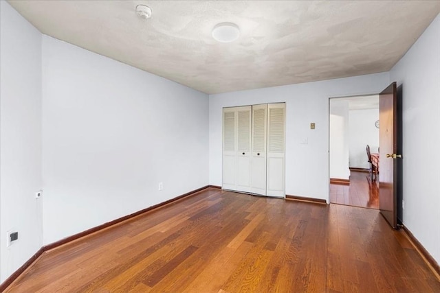 unfurnished bedroom featuring baseboards, wood finished floors, and a closet