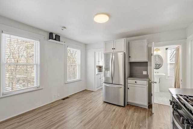 kitchen with stainless steel refrigerator with ice dispenser, white cabinets, light wood-type flooring, and range with gas stovetop