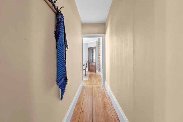 hallway featuring crown molding, light wood-type flooring, and baseboards