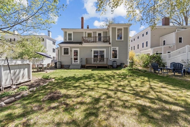 rear view of house featuring a deck, fence, a balcony, a yard, and a chimney