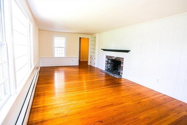 spare room with a baseboard heating unit, a healthy amount of sunlight, and hardwood / wood-style flooring