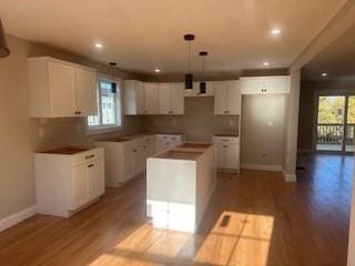 kitchen featuring pendant lighting, light hardwood / wood-style flooring, decorative backsplash, a kitchen island, and white cabinetry