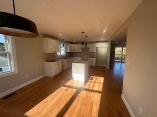 kitchen featuring a wealth of natural light, decorative light fixtures, hardwood / wood-style flooring, white cabinets, and a kitchen island