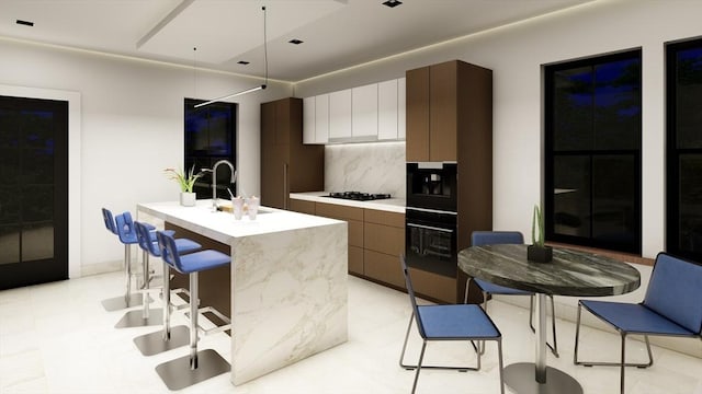 kitchen with sink, a kitchen island with sink, backsplash, black appliances, and white cabinets