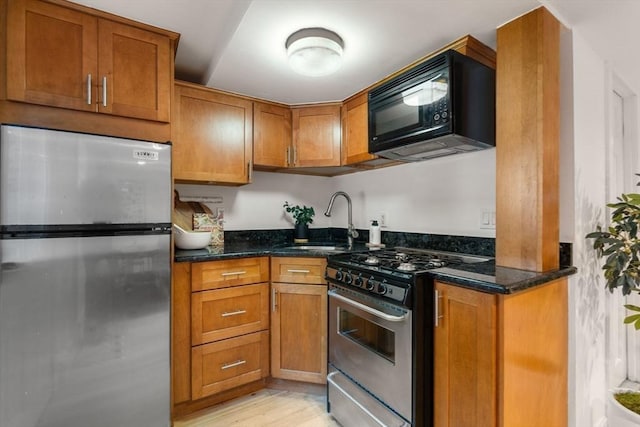 kitchen featuring light hardwood / wood-style floors, sink, stainless steel appliances, and dark stone counters