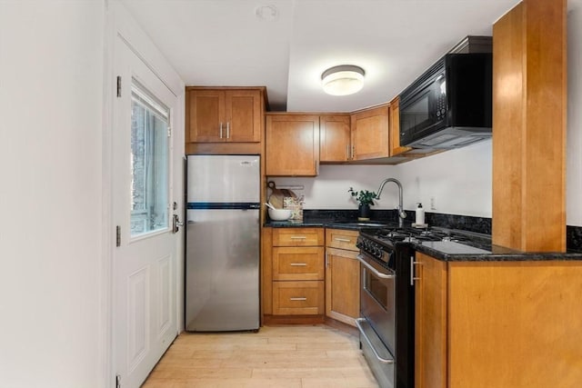 kitchen featuring appliances with stainless steel finishes, sink, dark stone countertops, and light hardwood / wood-style floors