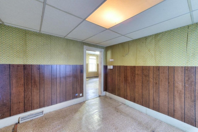 empty room with a wainscoted wall, wood walls, a paneled ceiling, and wallpapered walls