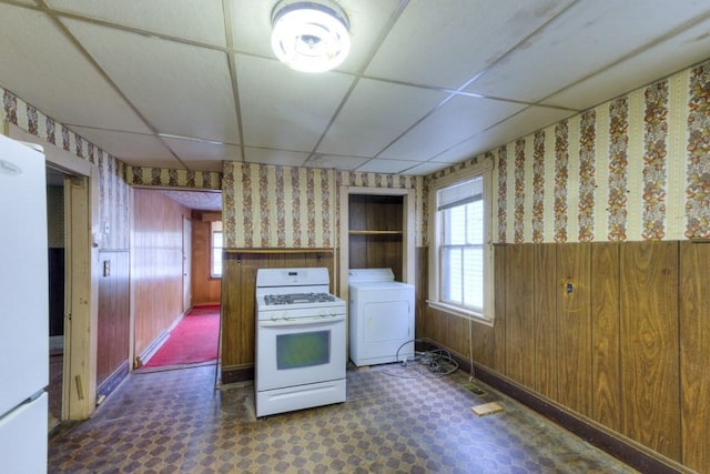 kitchen featuring washer / dryer, white appliances, wallpapered walls, dark flooring, and a drop ceiling