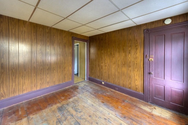 unfurnished room featuring a drop ceiling, wooden walls, and hardwood / wood-style floors
