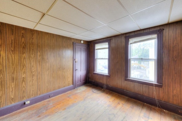 spare room featuring light wood-type flooring, wood walls, and a drop ceiling