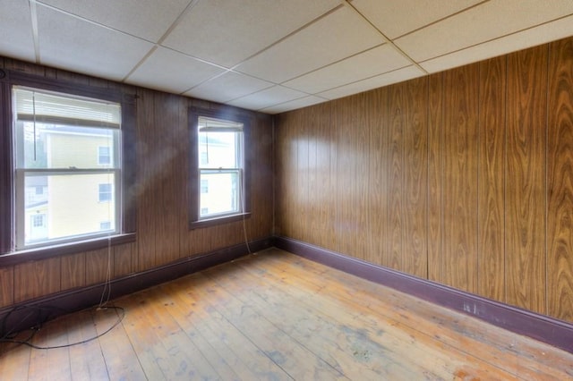 empty room featuring hardwood / wood-style floors, a drop ceiling, and wood walls