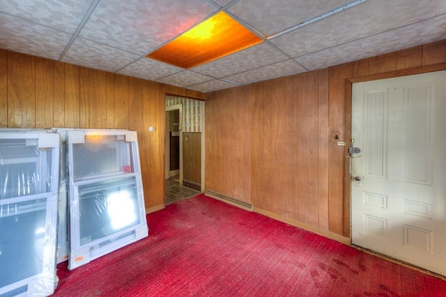 carpeted empty room featuring wood walls and a baseboard heating unit
