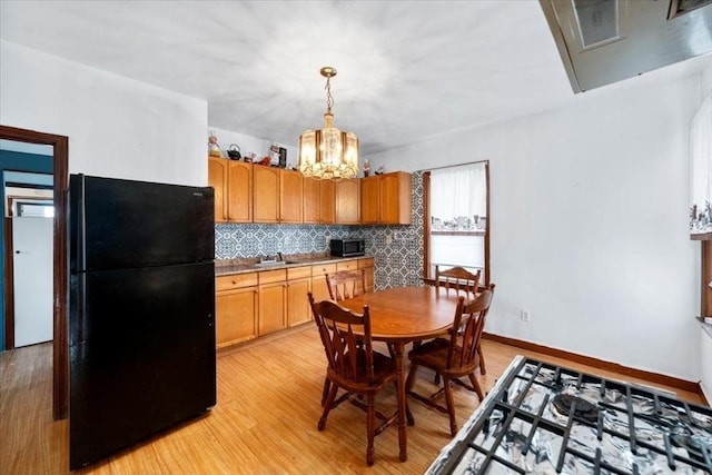 kitchen featuring sink, black fridge, backsplash, pendant lighting, and light wood-type flooring