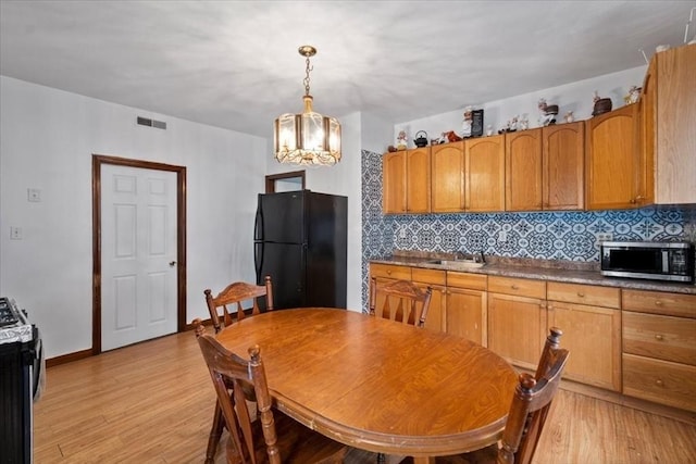 kitchen with decorative backsplash, light wood-type flooring, stainless steel appliances, and hanging light fixtures