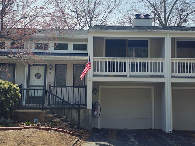 townhome / multi-family property featuring a chimney, a shingled roof, driveway, and an attached garage