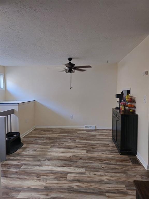 spare room with ceiling fan, visible vents, baseboards, a textured ceiling, and wood finished floors