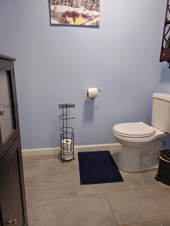 half bathroom with toilet, tile patterned flooring, and baseboards