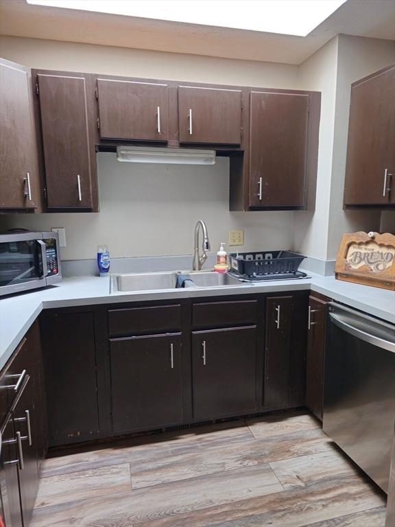 kitchen with a sink, stainless steel appliances, dark brown cabinets, light countertops, and light wood-type flooring