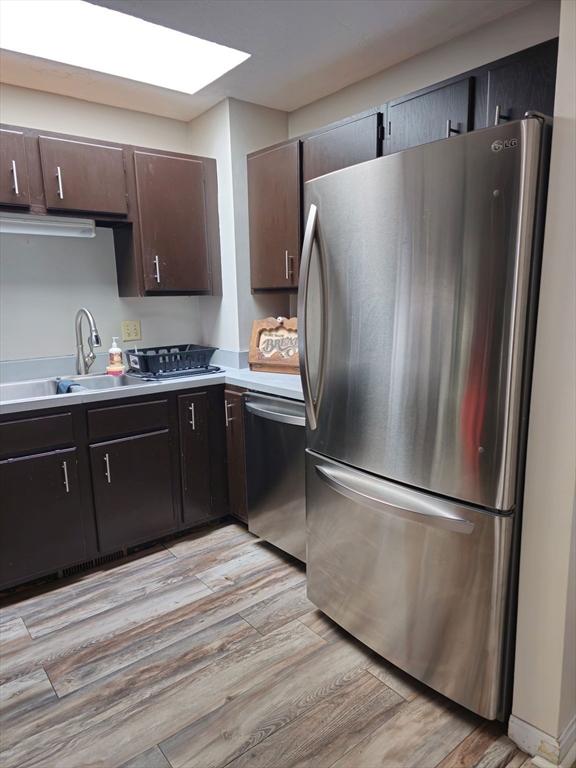 kitchen featuring light wood-style flooring, a sink, stainless steel appliances, light countertops, and a skylight