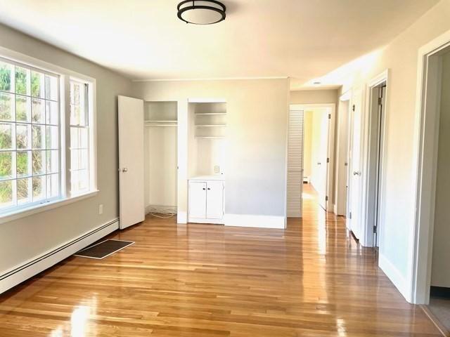 unfurnished bedroom featuring light hardwood / wood-style floors, a baseboard radiator, and two closets