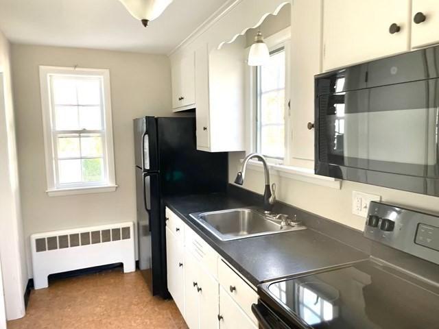 kitchen with white cabinets, electric range, sink, and radiator heating unit