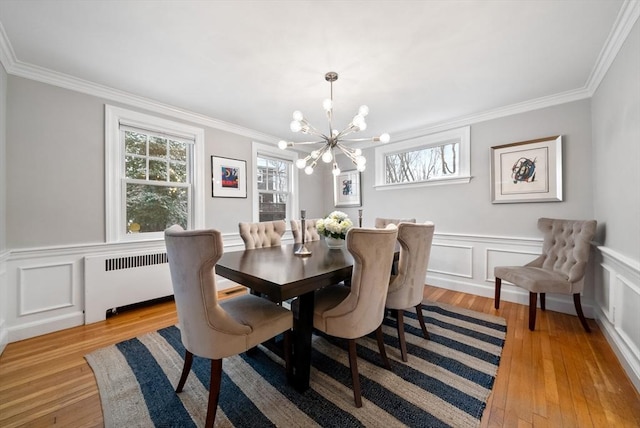 dining space with radiator heating unit, ornamental molding, light wood-type flooring, and a notable chandelier