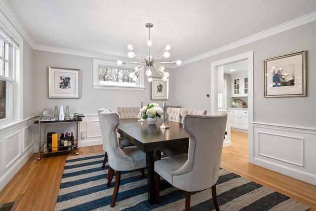 dining area with crown molding, light hardwood / wood-style flooring, and an inviting chandelier