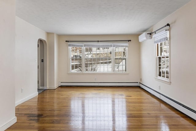 spare room featuring hardwood / wood-style floors, a baseboard radiator, and an AC wall unit