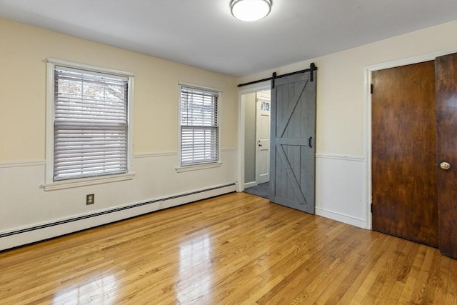 unfurnished bedroom with a barn door, a baseboard heating unit, and light hardwood / wood-style flooring