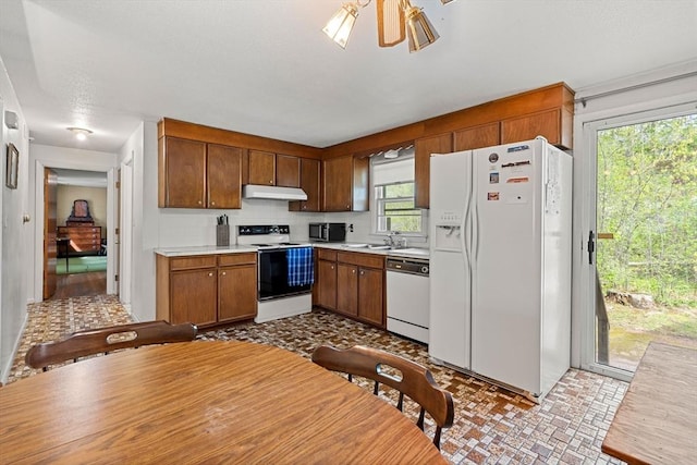 kitchen with white appliances, a sink, under cabinet range hood, light countertops, and tasteful backsplash