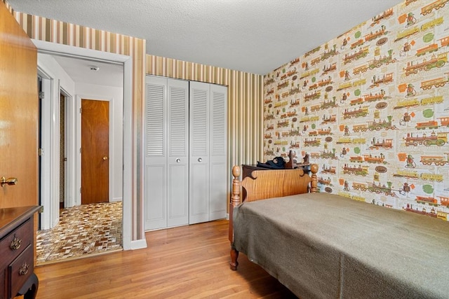 bedroom with wallpapered walls, light wood finished floors, a closet, and a textured ceiling