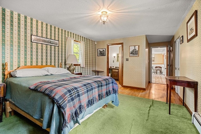carpeted bedroom with wallpapered walls, a baseboard heating unit, wood finished floors, and a textured ceiling
