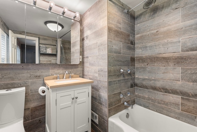 full bathroom with tile walls, oversized vanity, toilet, and tiled shower / bath combo