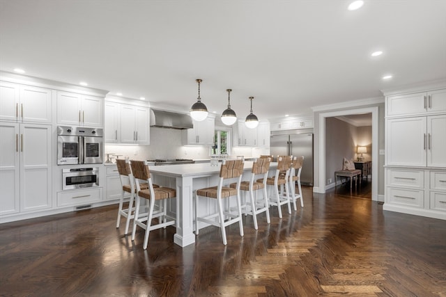 kitchen featuring a center island, wall chimney exhaust hood, stainless steel appliances, pendant lighting, and dark parquet floors