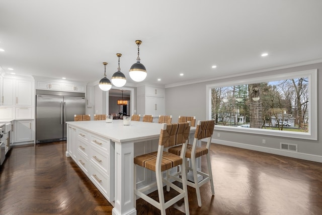 kitchen with a center island, built in fridge, crown molding, dark parquet flooring, and pendant lighting