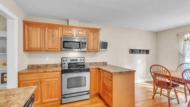 kitchen featuring a textured ceiling, light hardwood / wood-style floors, and stainless steel appliances