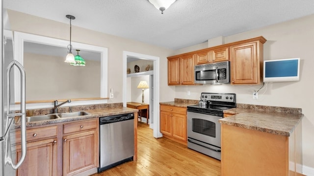 kitchen featuring stainless steel appliances, decorative light fixtures, a textured ceiling, sink, and light hardwood / wood-style floors