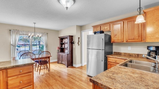 kitchen featuring stainless steel refrigerator, pendant lighting, sink, light hardwood / wood-style floors, and a chandelier