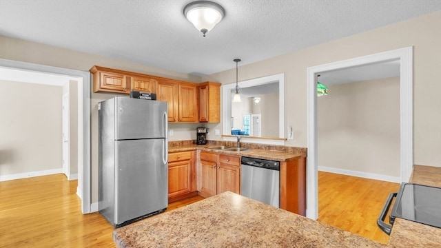 kitchen with sink, appliances with stainless steel finishes, a textured ceiling, decorative light fixtures, and light hardwood / wood-style flooring