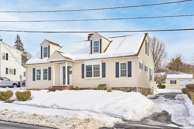 cape cod-style house featuring a chimney, a storage unit, and an outbuilding