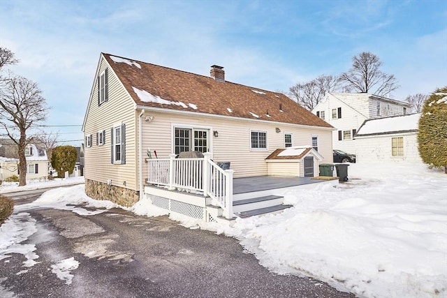 snow covered house featuring a deck, a shingled roof, and a chimney