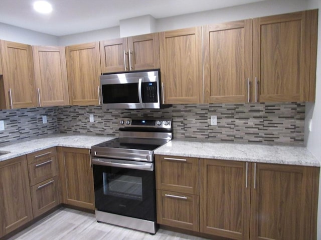 kitchen featuring stainless steel appliances, light stone countertops, light hardwood / wood-style floors, and decorative backsplash