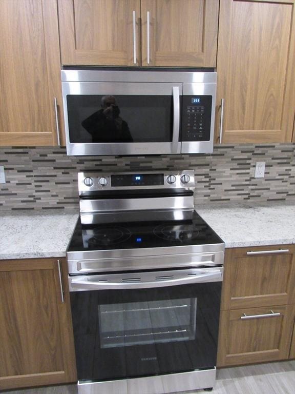 kitchen with decorative backsplash, light stone countertops, and appliances with stainless steel finishes