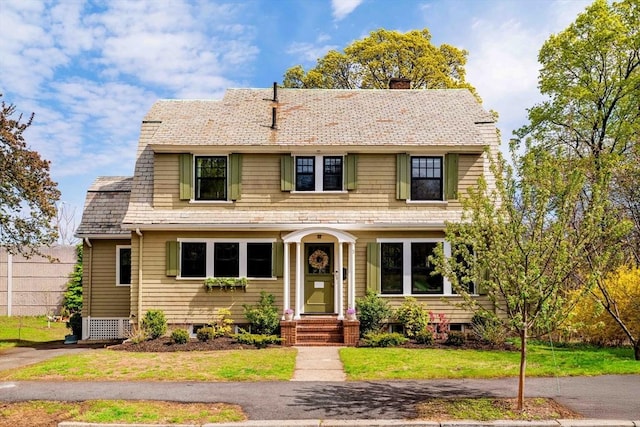 view of front of property featuring a gambrel roof, a front lawn, and a chimney