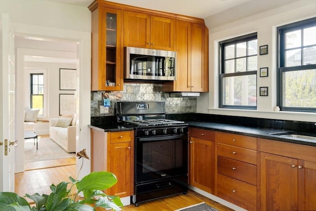kitchen with stainless steel microwave, brown cabinetry, light wood-style floors, and black gas range