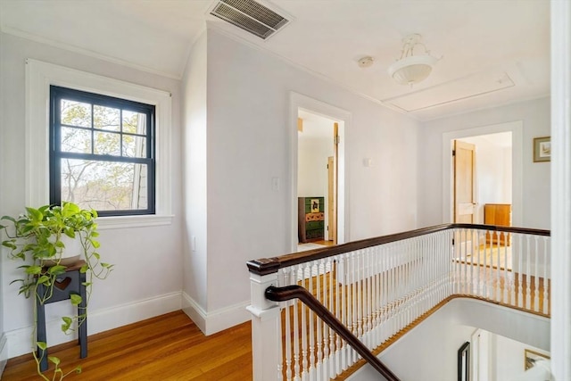 corridor featuring visible vents, wood finished floors, baseboards, attic access, and an upstairs landing
