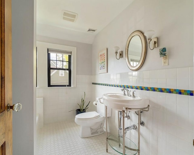 bathroom with visible vents, a wainscoted wall, toilet, and tile walls