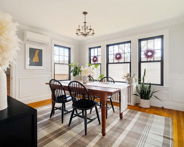 dining area with an inviting chandelier, a wall unit AC, crown molding, a wainscoted wall, and light wood-style floors