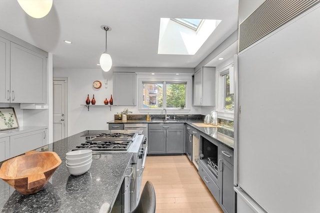 kitchen with built in refrigerator, a sink, a skylight, gray cabinetry, and light wood-type flooring