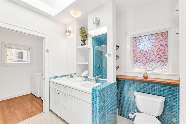 full bath featuring a stall shower, washing machine and clothes dryer, toilet, double vanity, and wood finished floors